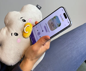 Ein Elternteil hält ein Smartphone auf dem Schoß, während daneben das graue Lenabie Plüschtier 