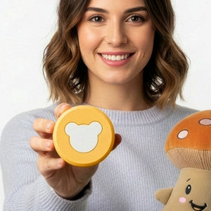 Mutter hält den Lenabo Smart Speaker in die Kamera und einen Lenabie in der anderen Hand. So zeigt sie, dass der kompakte und handliche Lenabo Smart Speaker überall hin mitgenommen werden kann und sich bequem in die Lenabies einsetzen lässt, um diese zu aktivieren und motivspezifische Audioerlebnisse für Kinder von 0-7 Jahren abzuspielen. Dabei erfolgt die Wiedergabe wahlweise bequem per Tastendruck am Lenabo Smart Speaker oder über die Lenabo App, in der Playlists erstellt und Sleep Timer gesetzt werden.